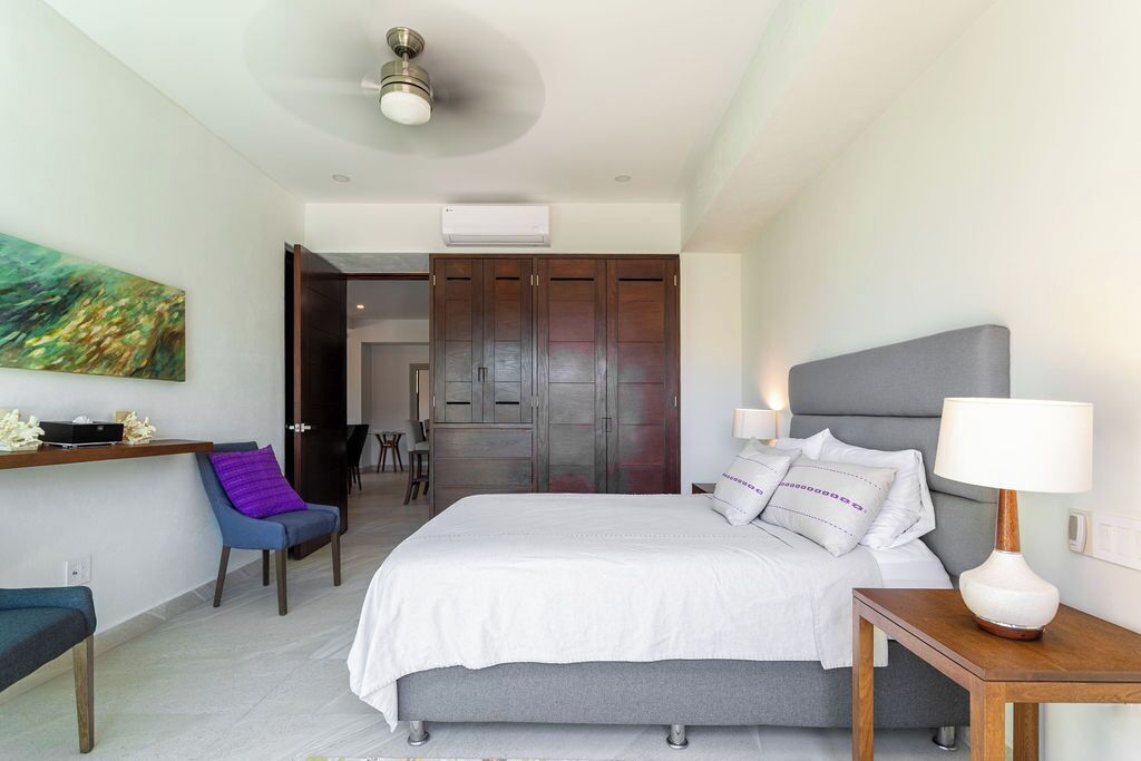 A modern bedroom with a bed, bedside table, chair, and artwork on the wall.