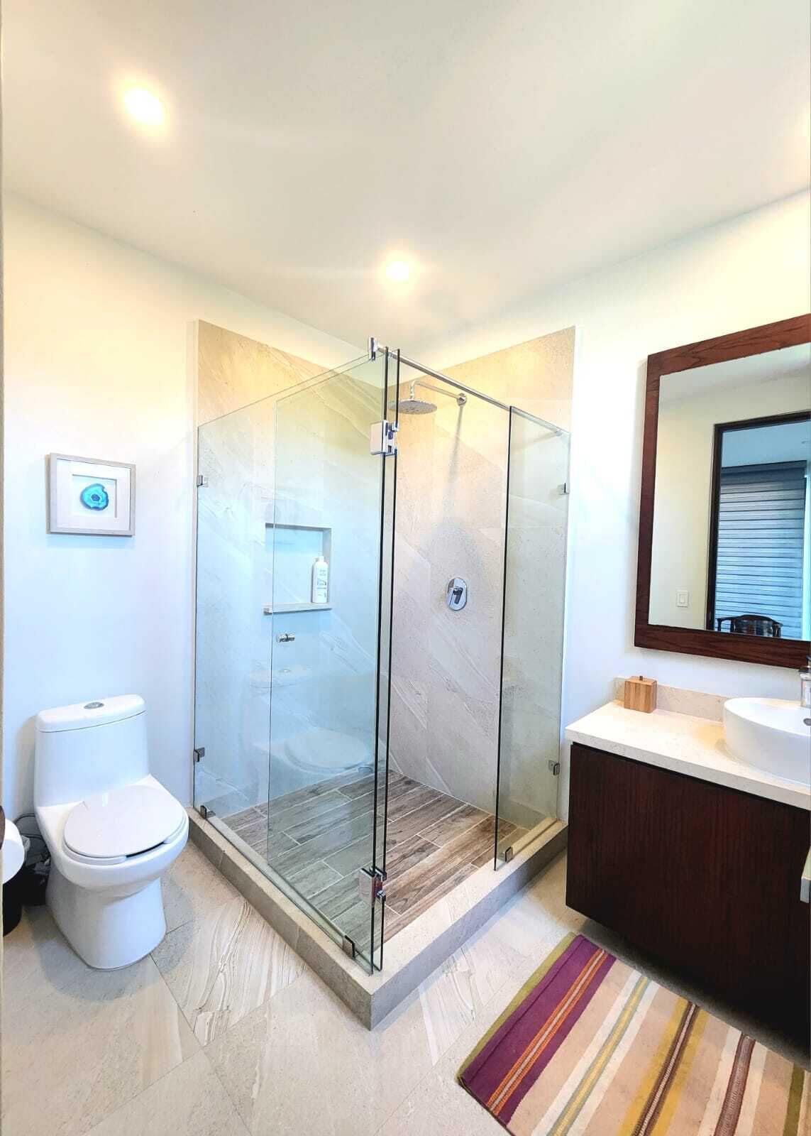 Un baño moderno con ducha separada por vidrio, inodoro y tocador con espejo.