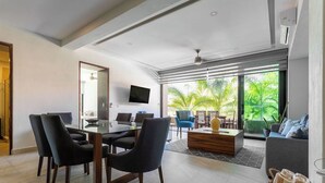 Una sala de estar moderna con comedor, ventanas grandes y vista a zonas verdes.