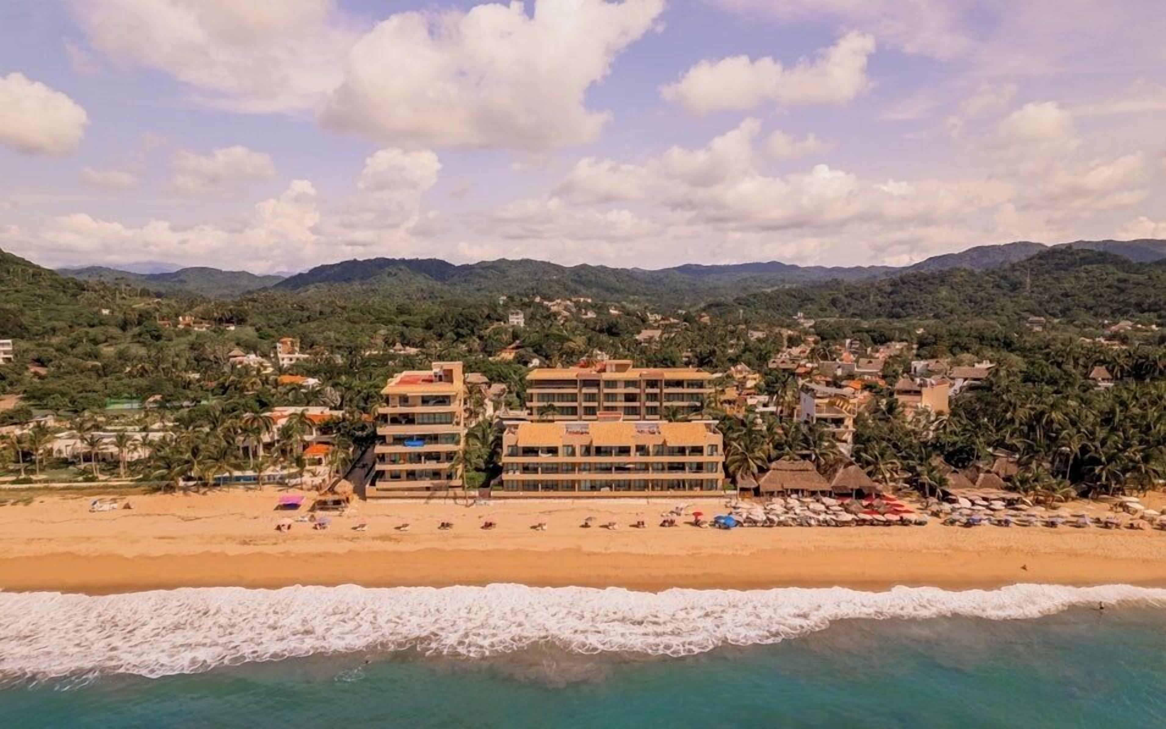 A coastal hotel with multiple floors, beachfront location, and a view of the sea and mountains.