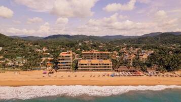 A coastal hotel with multiple floors, beachfront location, and a view of the sea and mountains.