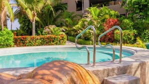 Piscina con pasamanos metálicos, rodeada de vegetación exuberante y palmeras.