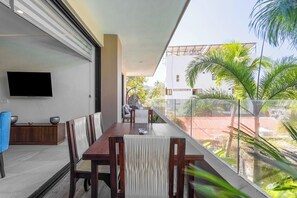 A dining area with a table and chairs, a flat-screen TV mounted on the wall, and a view of the outside through a glass railing. - Villa Orquídea (San Francisco)