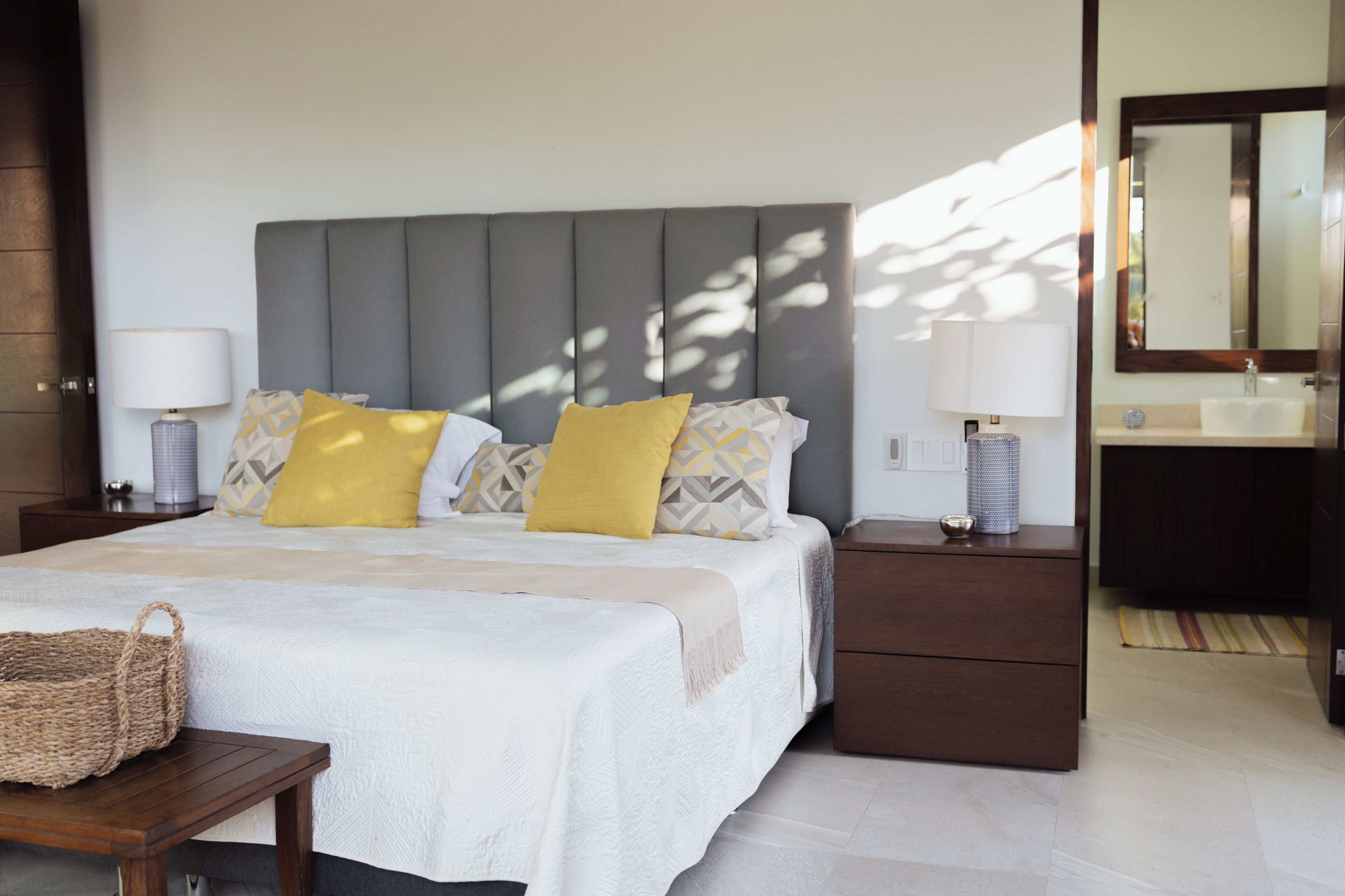 Habitación de hotel con cama, mesitas de noche, tocador, espejo y baño con lavabo y espejo.