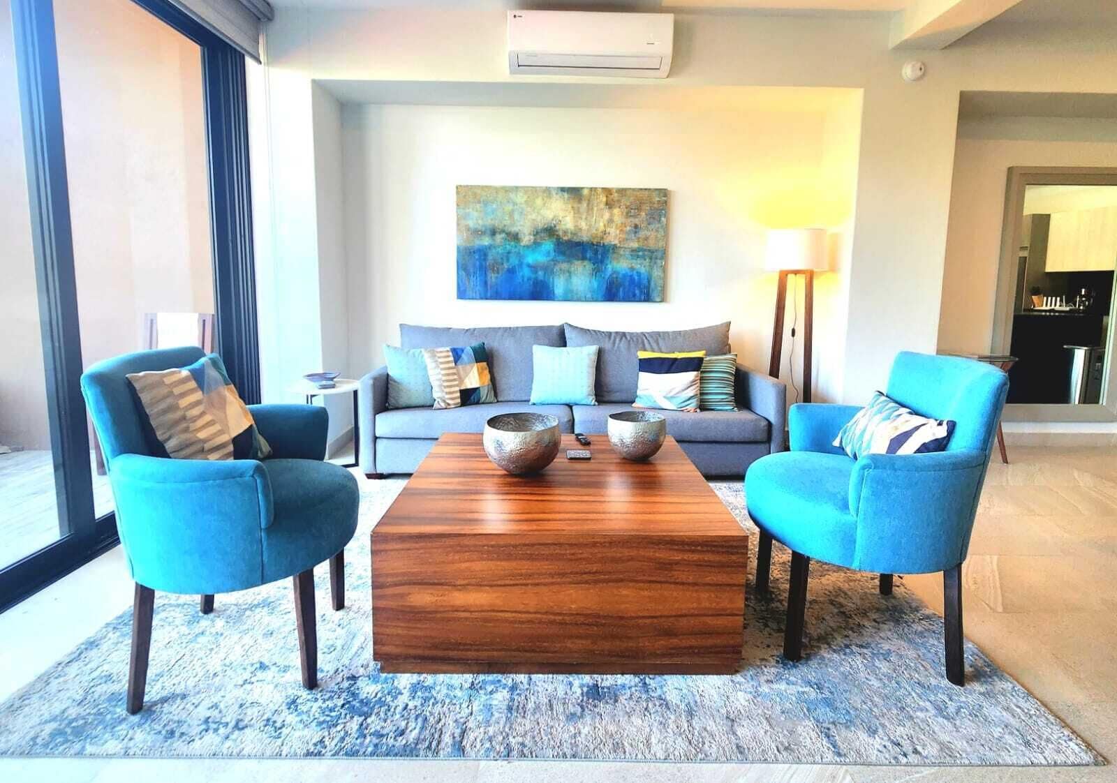 A modern living room with a sofa, two armchairs, a coffee table, and a painting on the wall.