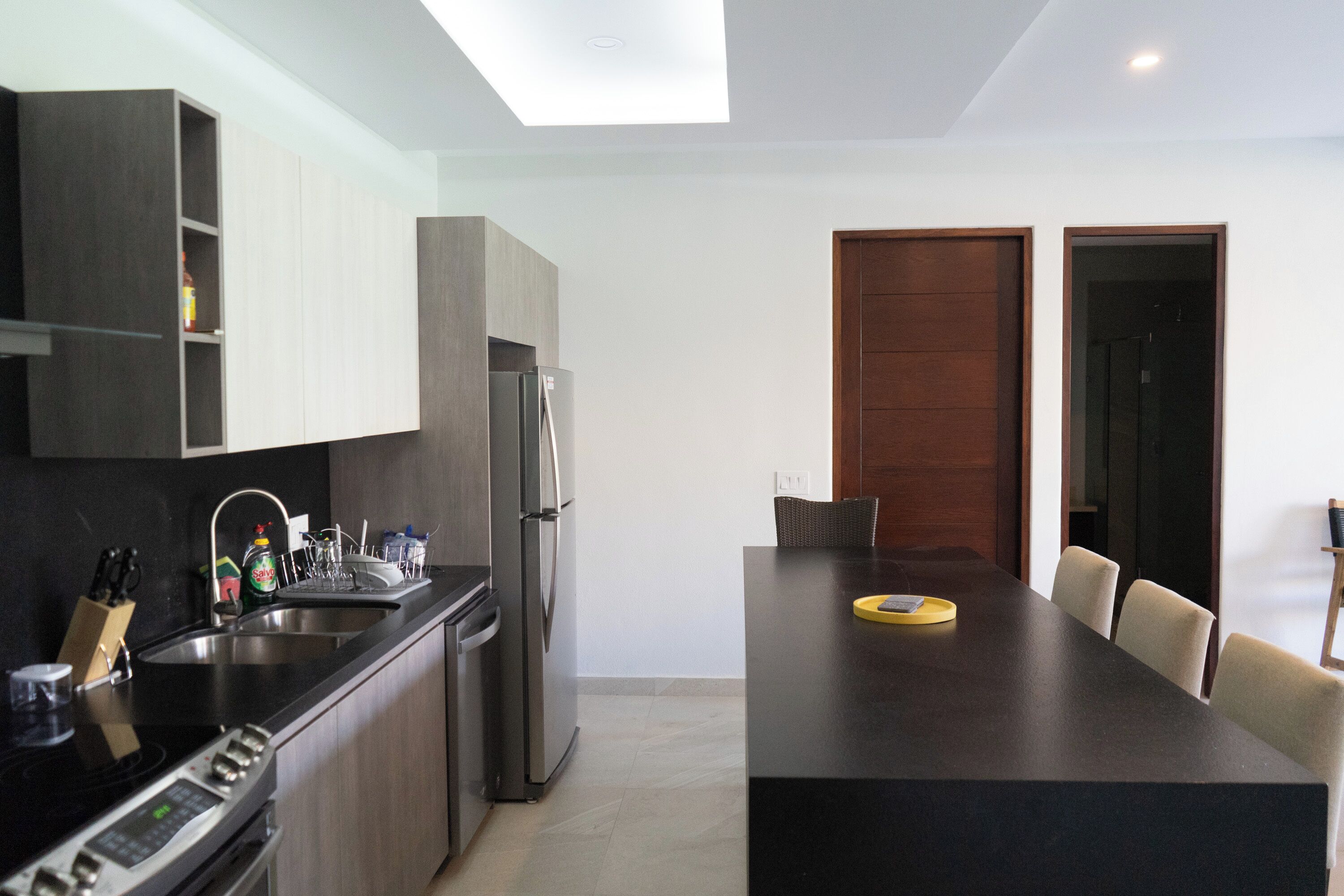 Una cocina moderna con una isla central, electrodomésticos integrados y un comedor con mesa y sillas oscuras.