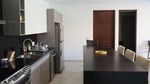 Una cocina moderna con una isla central, electrodomésticos integrados y un comedor con mesa y sillas oscuras.