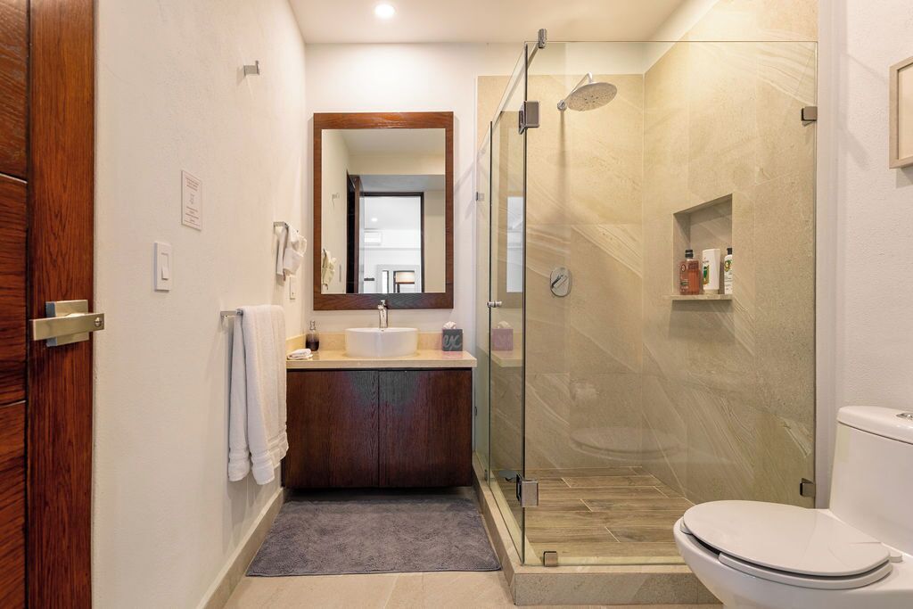 Un baño moderno con ducha de vidrio, lavamanos blanco y tocador de madera.