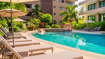 A pool area with lounge chairs and umbrellas, surrounded by greenery and a modern building.