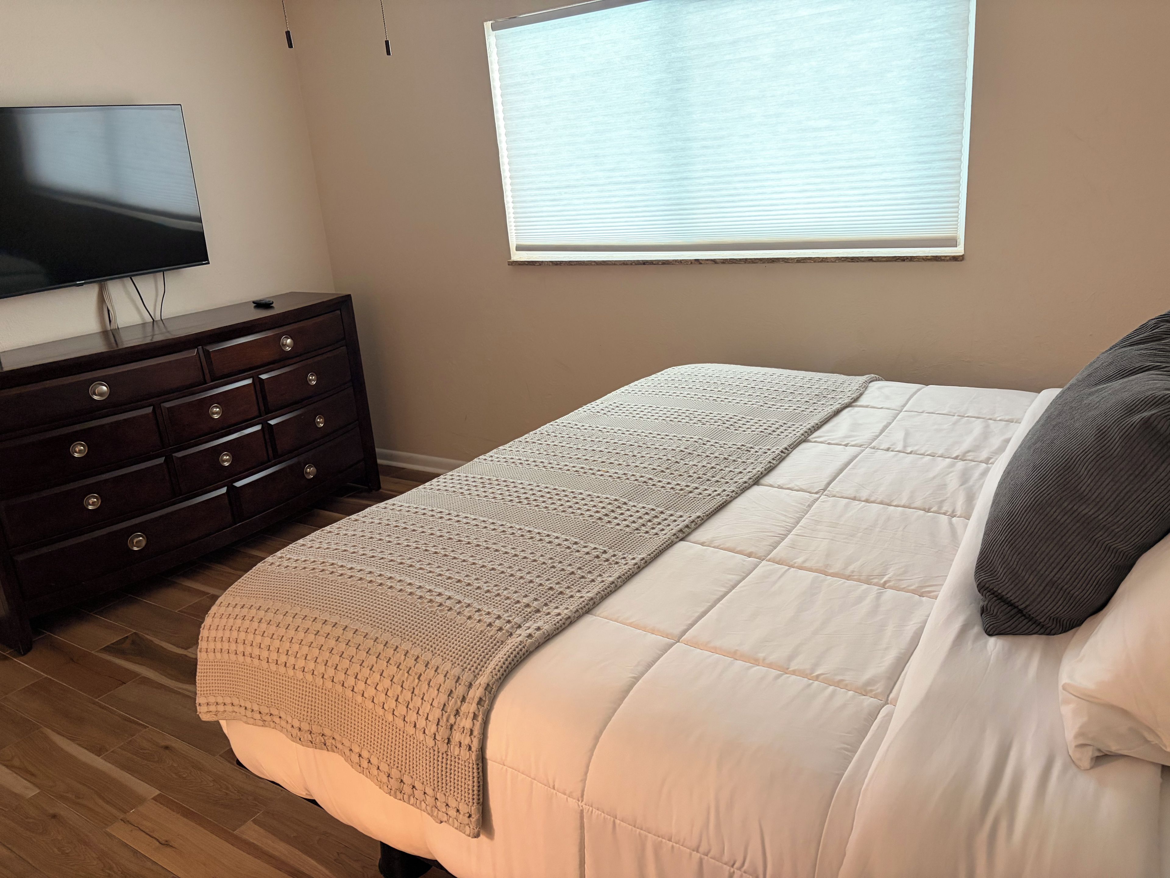 Un dormitorio con cama, cómoda, televisor y ventana.