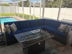 A covered patio area with a blue sectional sofa, a glass-top coffee table, and a wicker side table. - 3-bedroom house in peaceful Cape Coral with heated saltwater pool (Cape Coral)