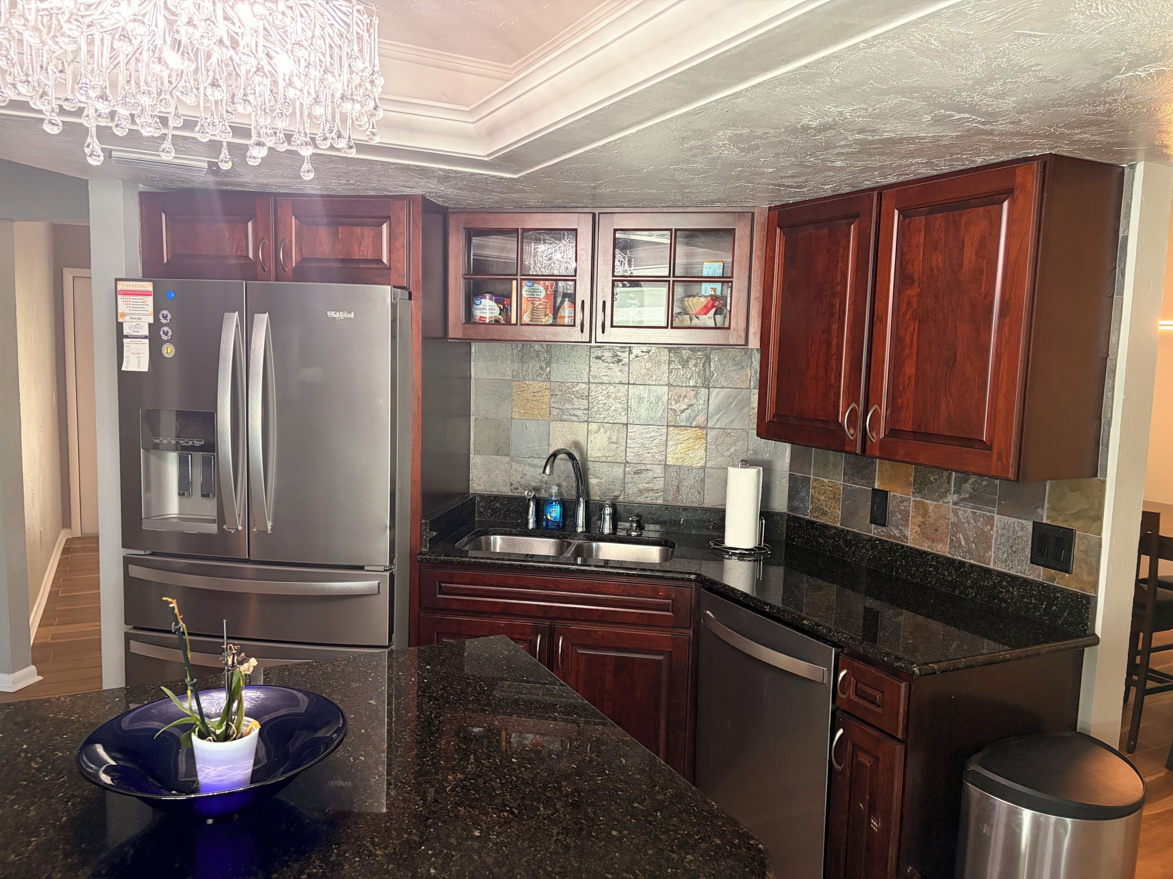 A modern kitchen with dark wood cabinets, a stainless steel refrigerator, a granite countertop, and a built-in dishwasher.