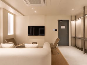 A modern hotel room with a large bed, a flat-screen TV mounted on the wall, and a door with a control panel.