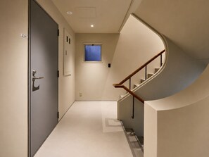 A hallway with a door, a window, and a curved staircase. - TORA HOTEL Ueno 5-chome  (Tokyo)