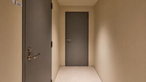 Um corredor com uma porta fechada no final, uma porta com maçaneta à esquerda e um luminário no teto.