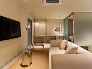 A modern hotel room with a flat-screen TV, a sofa, a small table, and a bathroom with a sink and mirror. - TORA HOTEL Ueno 5-chome  (Tokyo)