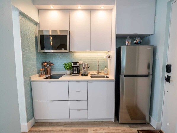 A compact kitchen with white cabinets, a stainless steel refrigerator, and a microwave.