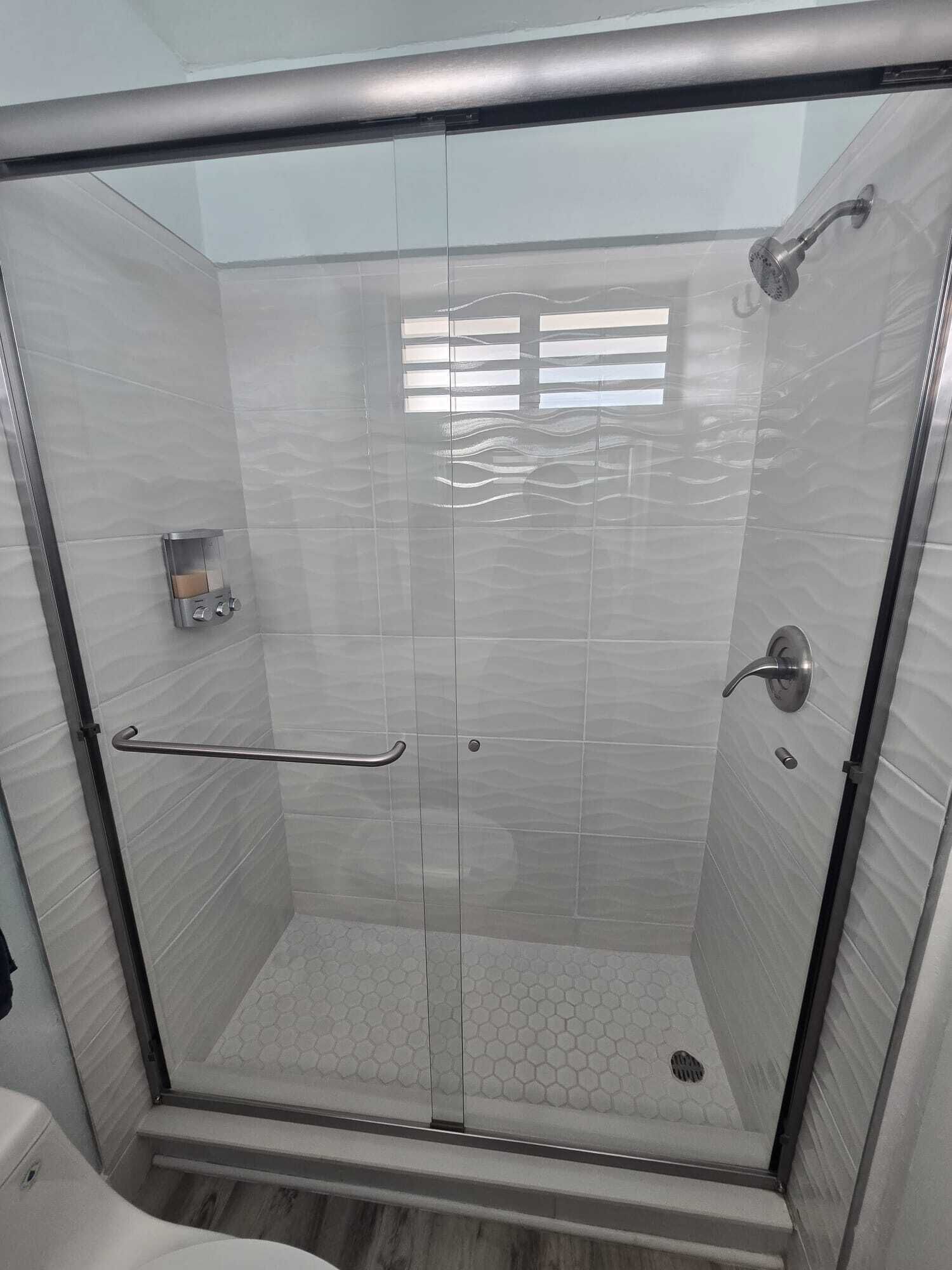 Une douche fermée par des parois en verre, dotée d’une barre d’appui, d’un panneau de commande et d’un sol carrelé.