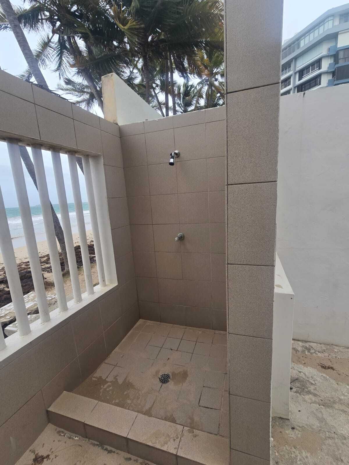 Un petit espace douche fermé, avec des murs carrelés et une pomme de douche en métal.
