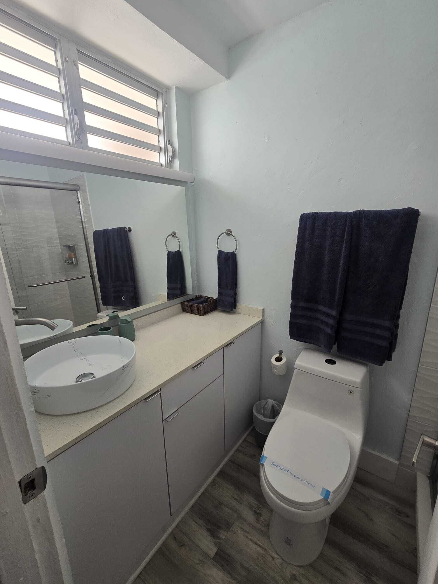 Een badkamer met een rond wastafel, toilet, spiegel en raam.