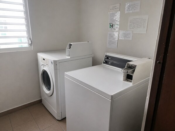 A laundry room with a front-loading washer and dryer, a window with blinds, and informational notices on the wall.