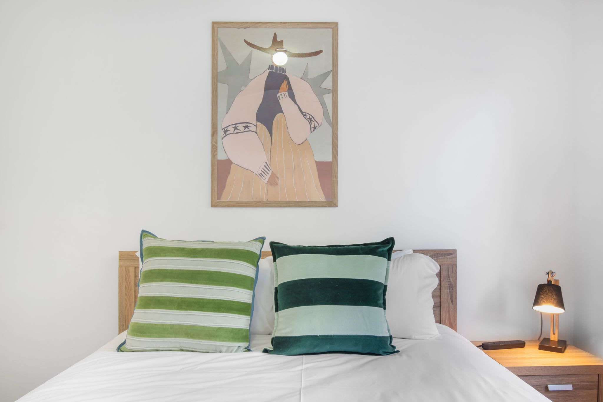 A bed with two pillows, a bedside table with a lamp, and a framed artwork on the wall.
