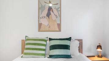 A bed with two pillows, a bedside table with a lamp, and a framed artwork on the wall.