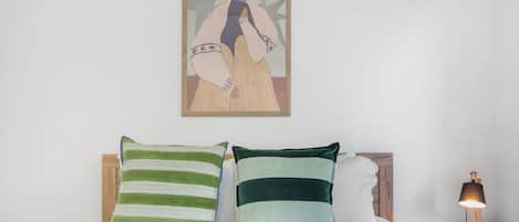 Un lit avec deux oreillers, une table de chevet avec une lampe et une œuvre d’art encadrée accrochée au mur.