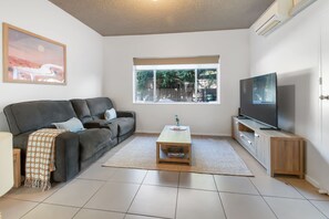 Un salon avec un canapé, une table basse, un téléviseur et une fenêtre donnant sur des arbres.
