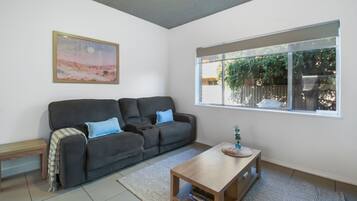 A living room with a sofa, a coffee table, a rug, a painting, and a window with a view of greenery.