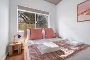 Une chambre à coucher avec un grand lit, deux oreillers, une table de chevet avec une lampe et une fenêtre donnant sur des arbres.