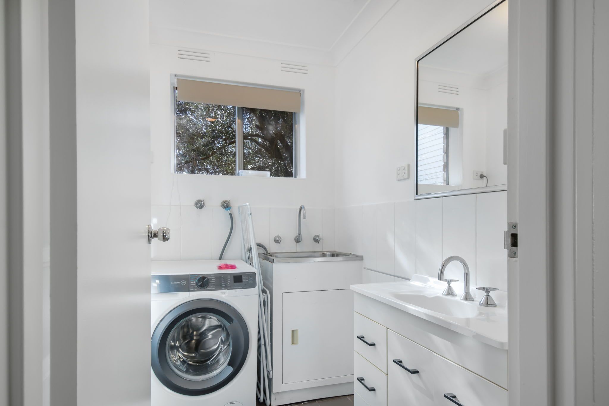 A modern bathroom with a washing machine, a sink, and a mirror.