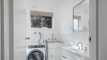 A modern bathroom with a washing machine, a sink, and a mirror.