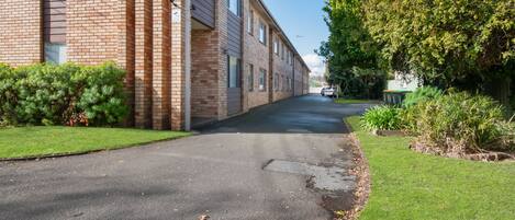 A residential street with a brick building on the left and a tree-lined driveway.