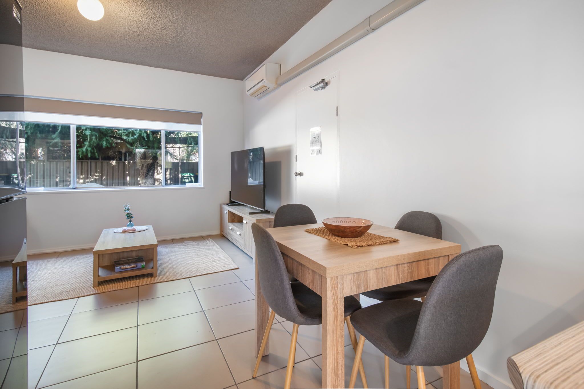 Une cuisine moderne avec un coin repas, un téléviseur et une fenêtre donnant sur les arbres.