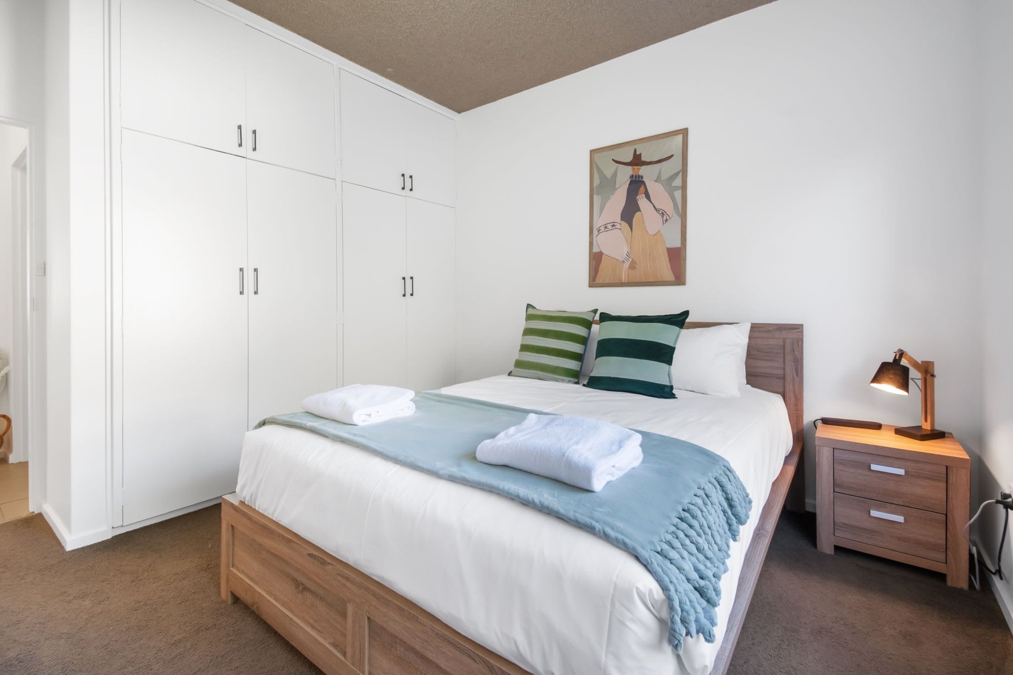 A bedroom with a bed, a nightstand, a lamp, a wardrobe, and a painting on the wall.