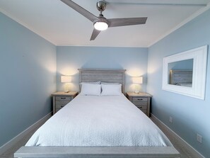 Ein Schlafzimmer mit einem Bett, zwei Nachttischen, einem Deckenventilator und einem an der Wand befestigten Spiegel.