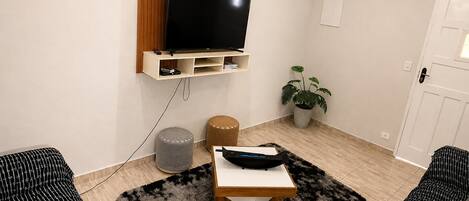 Una sala de estar moderna con un televisor de pantalla plana, un panel de pared de madera, una planta en maceta, un otoman redonda y una alfombra blanco y negro.