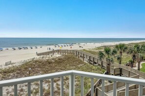 Ein Strand mit Holzsteg, Sonnenschirmen und freiem Blick auf das Meer.