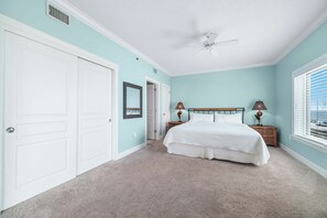 Ein Schlafzimmer mit Bett, Nachttisch, Lampe, Deckenventilator und einem Fenster mit Jalousien.