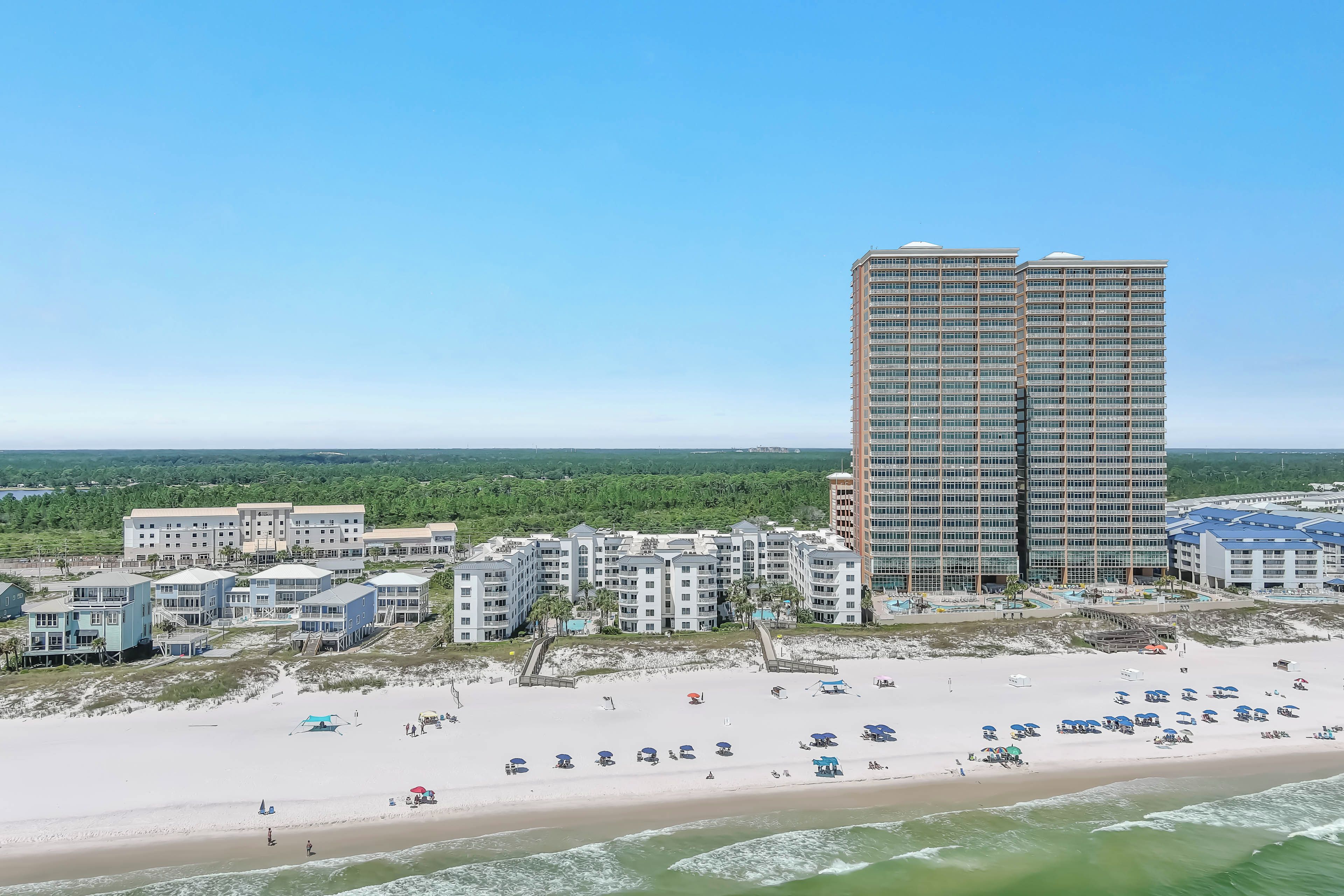 A beachfront hotel with multiple buildings, a sandy beach, and a clear sky.