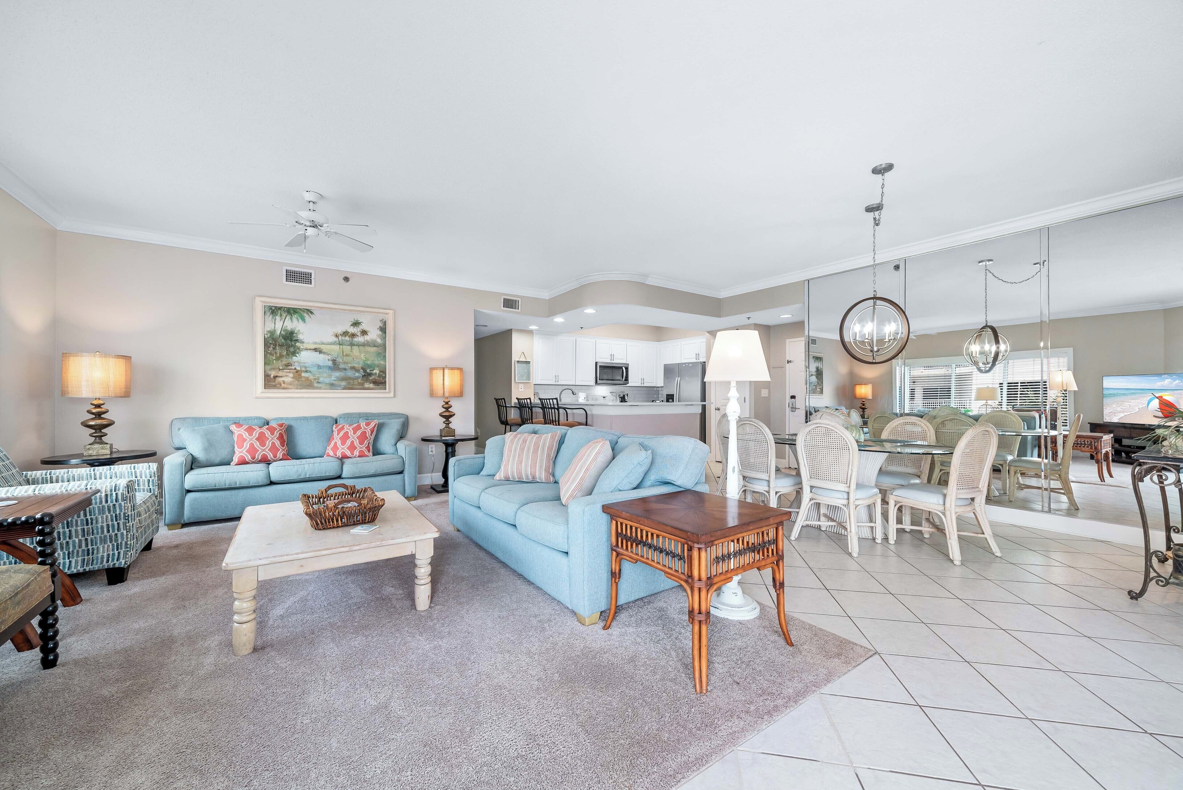A spacious living room with a blue sofa, a coffee table, and a dining area with wicker chairs.
