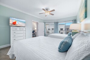 A hotel room with a bed, a ceiling fan, a TV, and a view of the outside. - Gulf-Front Views | Spacious 3BR | Beach Access & Pool | BEACHBALL PROPERTIES (Orange Beach)