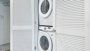 A laundry room with two stacked washing machines, a door, and a wall with horizontal lines. - Gulf-Front Views | Spacious 3BR | Beach Access & Pool | BEACHBALL PROPERTIES (Orange Beach)