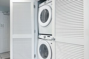 Ein Waschraum mit zwei übereinander gestapelten Waschmaschinen, einer Tür und einer Wand mit horizontalen Linien.