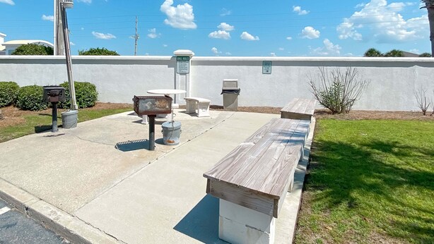 An outdoor seating area with concrete tables and benches, a trash can, and a sign indicating 'GRILL RULES'. - Gulf-Front Views | Spacious 3BR | Beach Access & Pool | BEACHBALL PROPERTIES (Orange Beach)