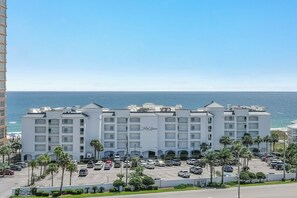 A multi-story hotel with a beachfront view, featuring a parking lot and palm trees. - Gulf-Front Views | Spacious 3BR | Beach Access & Pool | BEACHBALL PROPERTIES (Orange Beach)