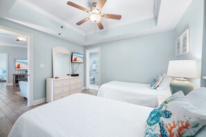 Ein Schlafzimmer mit zwei Betten, einem Deckenventilator, einem Fernseher und einem durchgehenden Türrahmen sichtbaren Badezimmer.