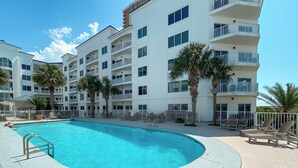 A hotel with a swimming pool, multiple balconies, and palm trees. - Gulf-Front Views | Spacious 3BR | Beach Access & Pool | BEACHBALL PROPERTIES (Orange Beach)