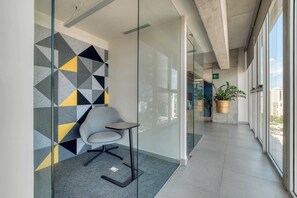 An office space with a modern chair, geometric wall design, and a view of the city through large windows. - Providencia Deluxe Studio in Brand-New Building (Guadalajara)